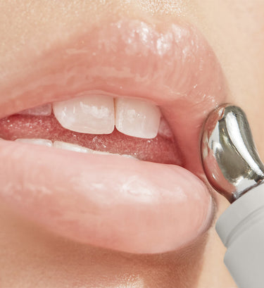 Close-up of lips and teeth with metal applicator tool showing cosmetic product application.