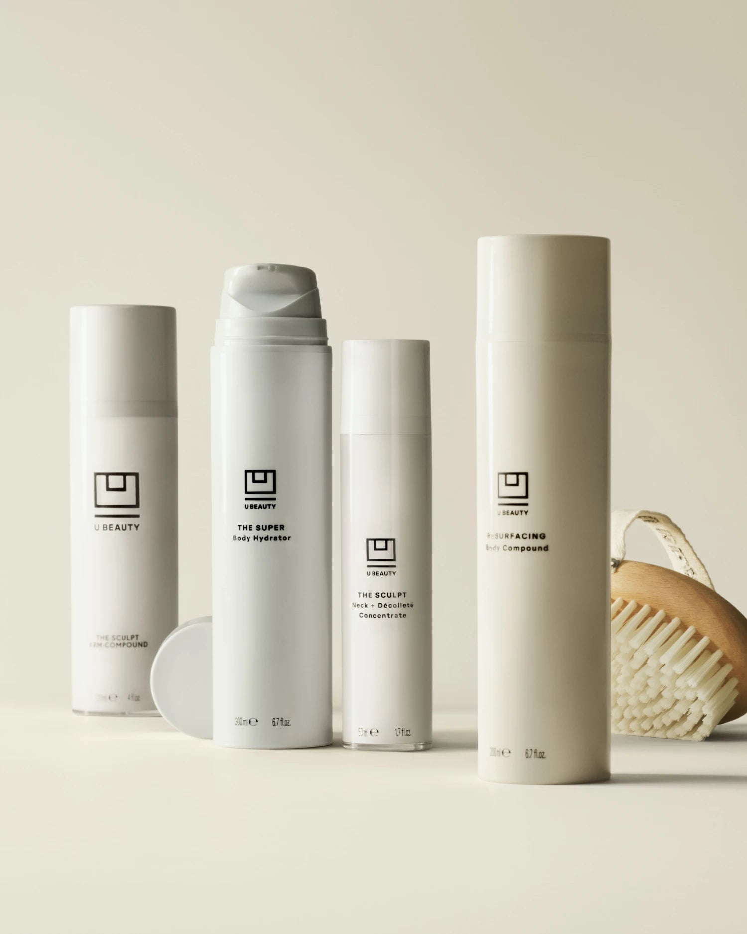 Quatre flacons cylindriques blancs de produits de soin pour la peau portant la marque U Beauty, accompagnés d'un panier tressé, disposés sur un fond beige neutre