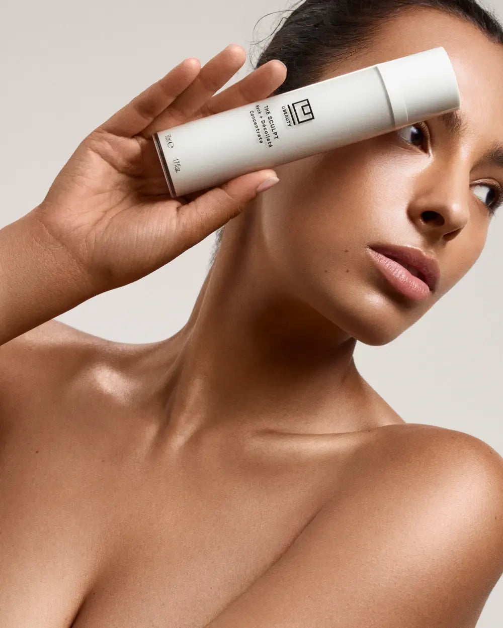 Flacon cylindrique blanc de concentré, placé près du cou et du décolleté d'une femme.