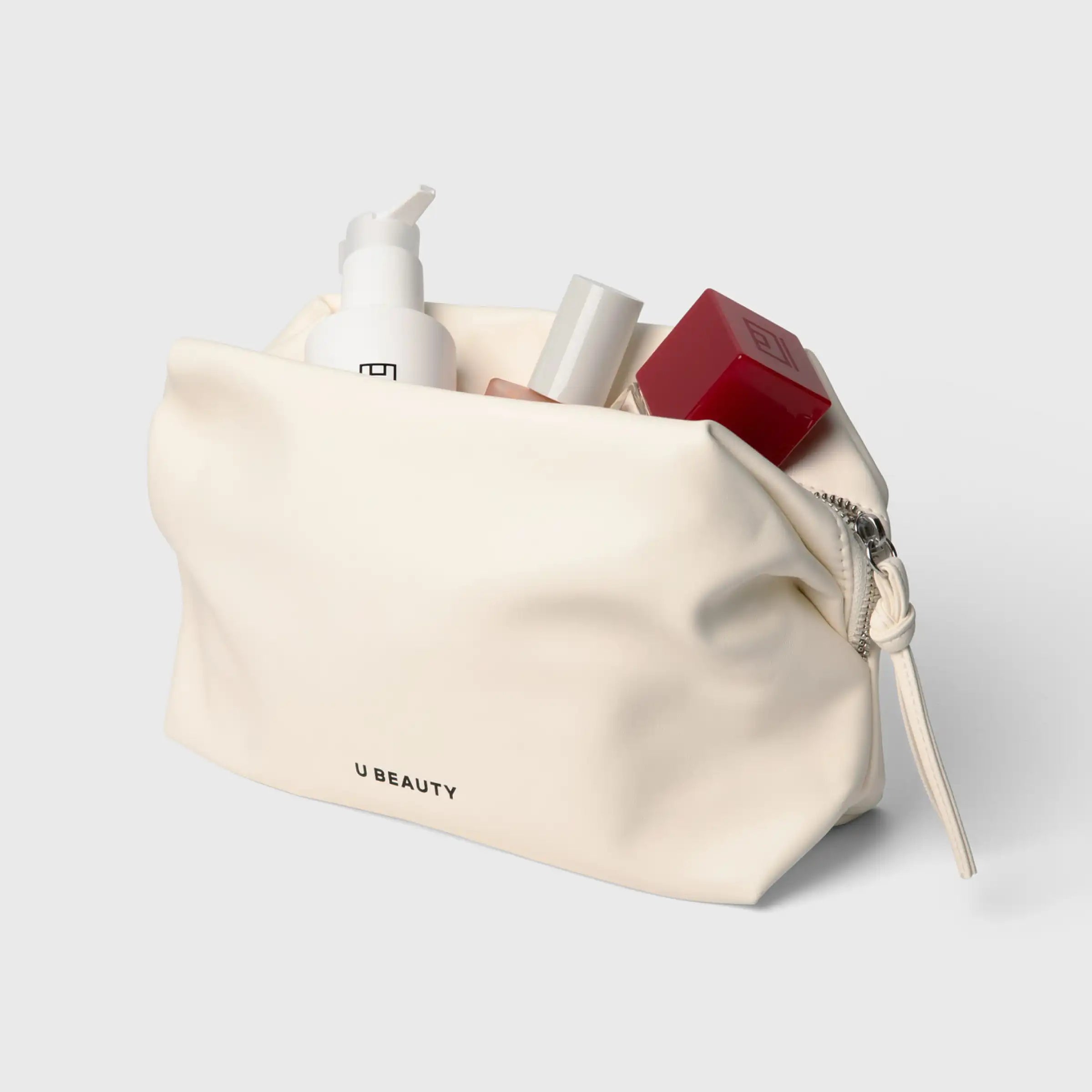 Cream-colored cosmetic bag with zippered top containing skincare and beauty products including pump bottle, cylindrical conta