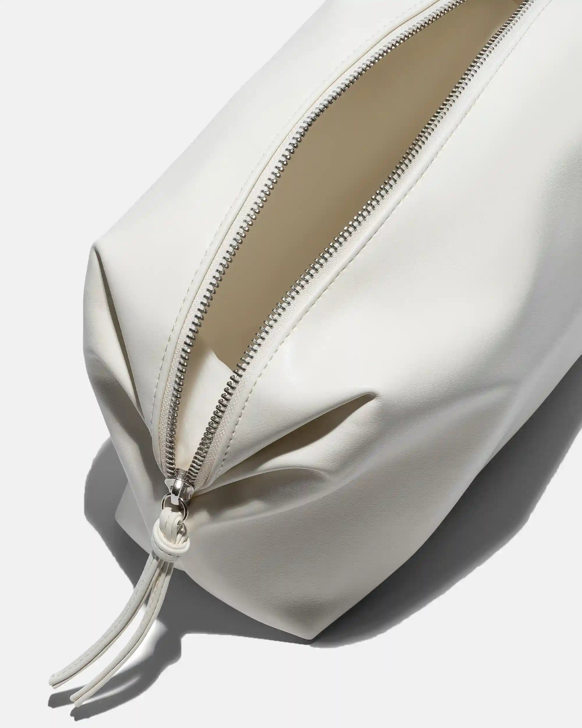 Bolsita de piel blanca con cremallera plateada y detalle de borla, que se muestra abierta para mostrar su interior de color beige.