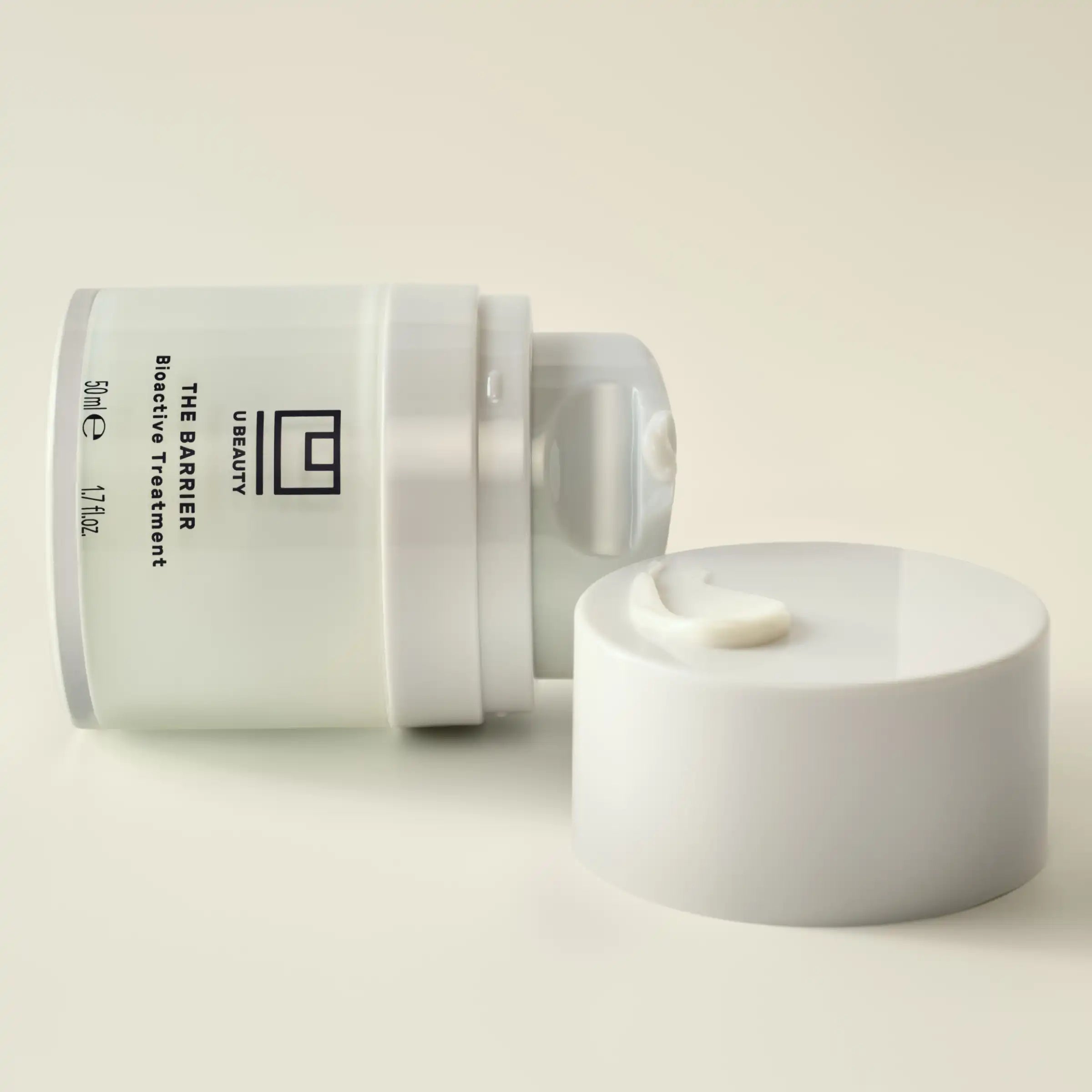 White cylindrical jar of The BARRIER Bioactive Treatment with matching lid and creamy product sample displayed on white surfa