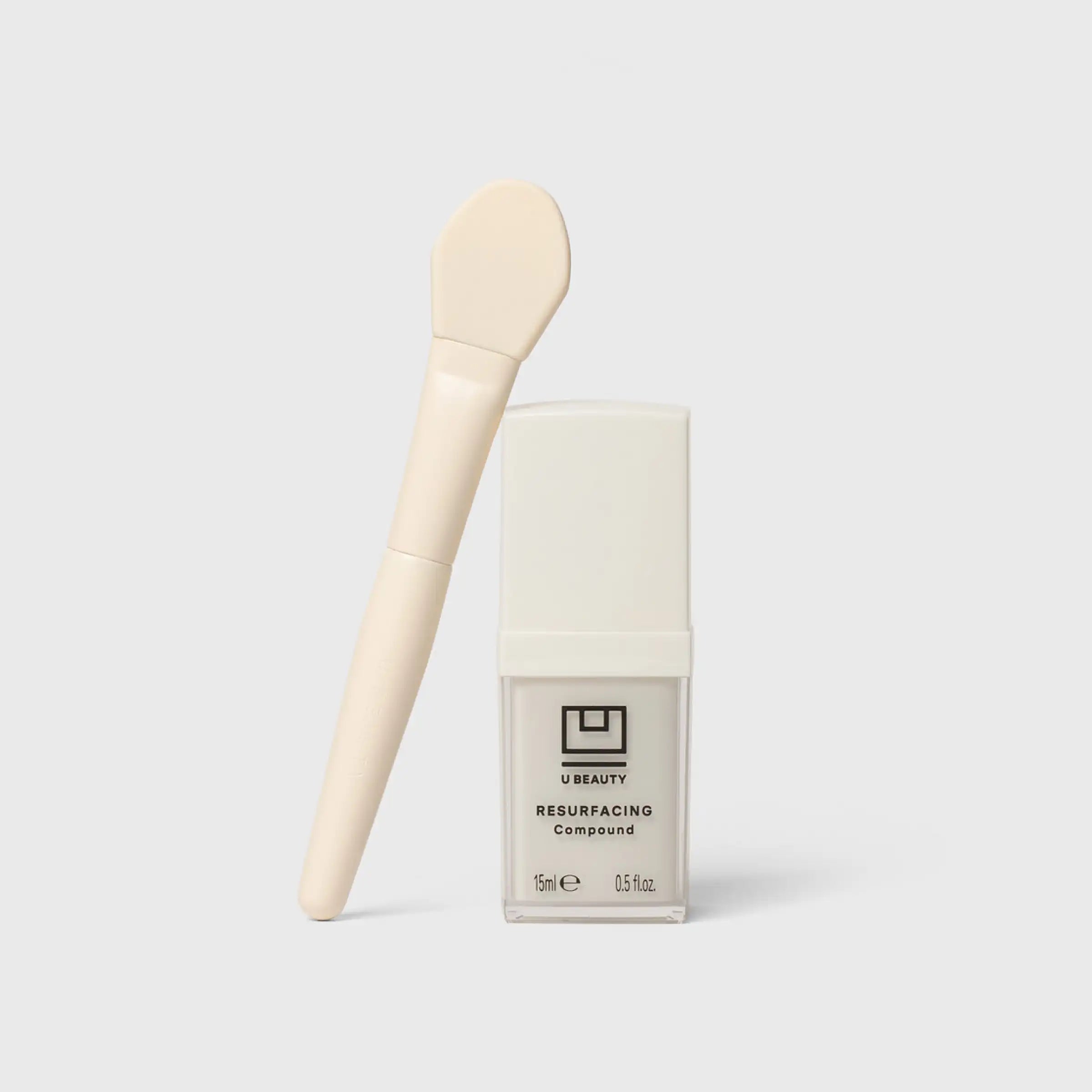 Cream-colored brush with rounded head and wooden handle, positioned next to white U Beauty Resurfacing Compound bottle.