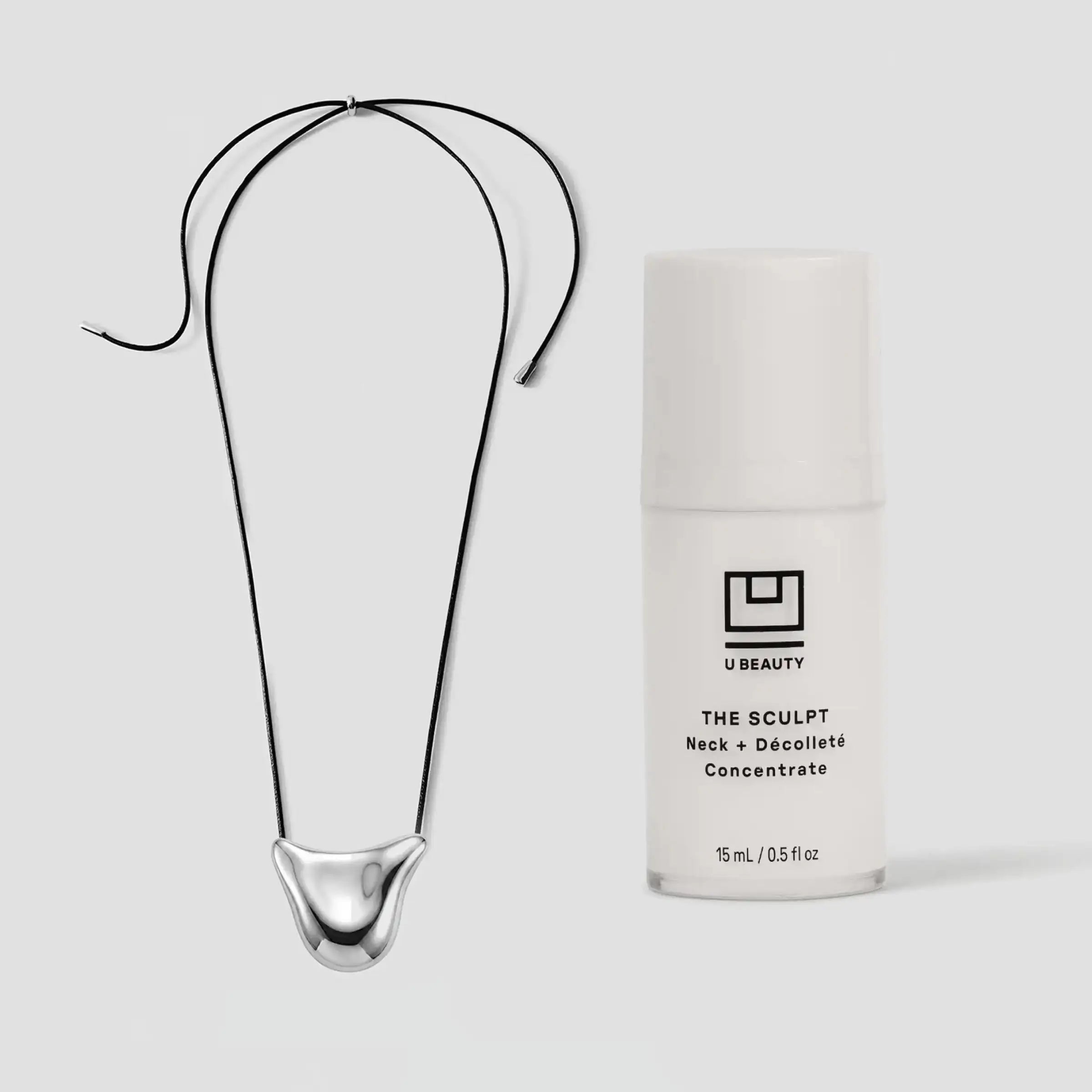 Collier en métal noir incurvé, orné d'un pendentif sculptural, présenté à côté d'un flacon blanc de produit de beauté.