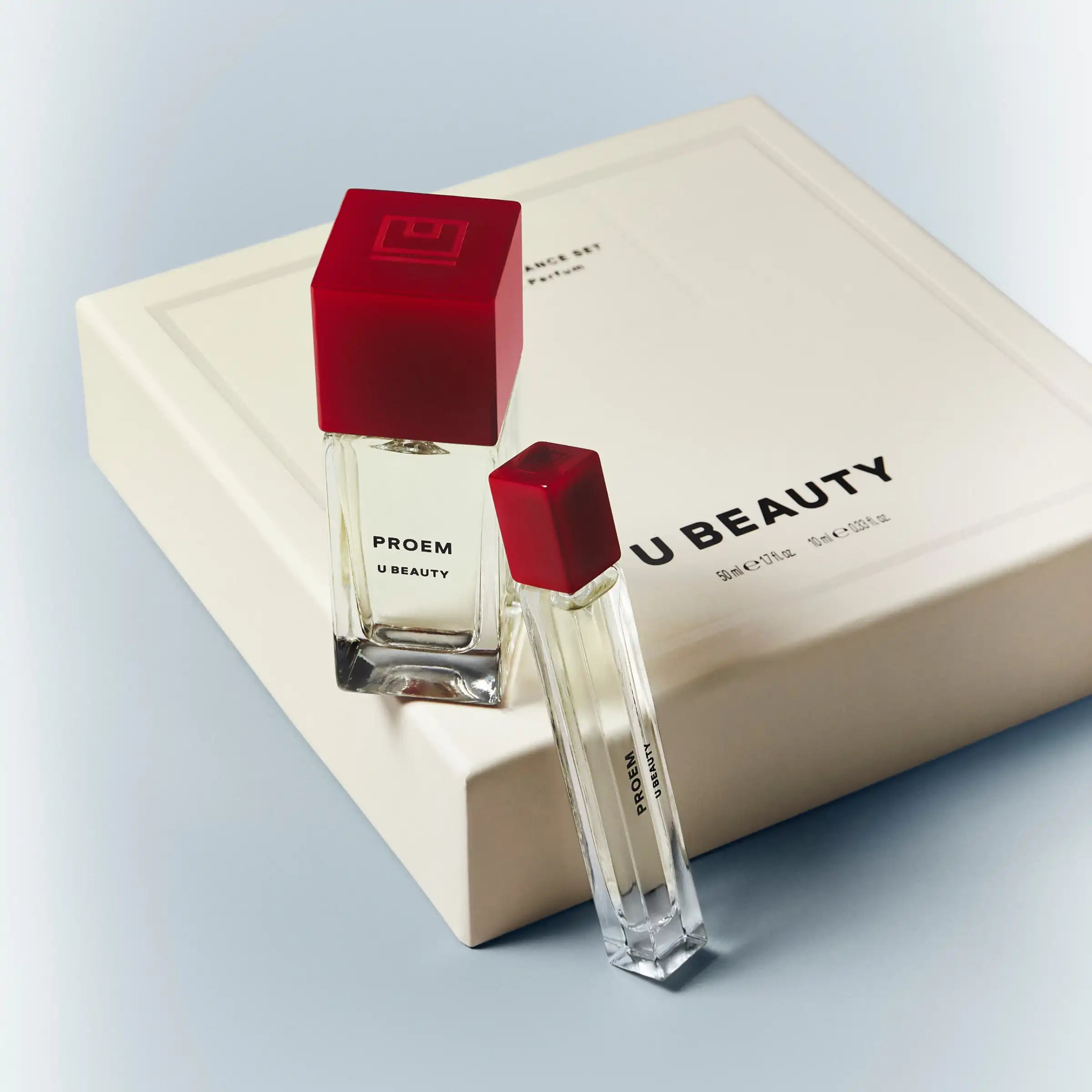 Two clear glass fragrance bottles with red square caps in a cream-colored box labeled 