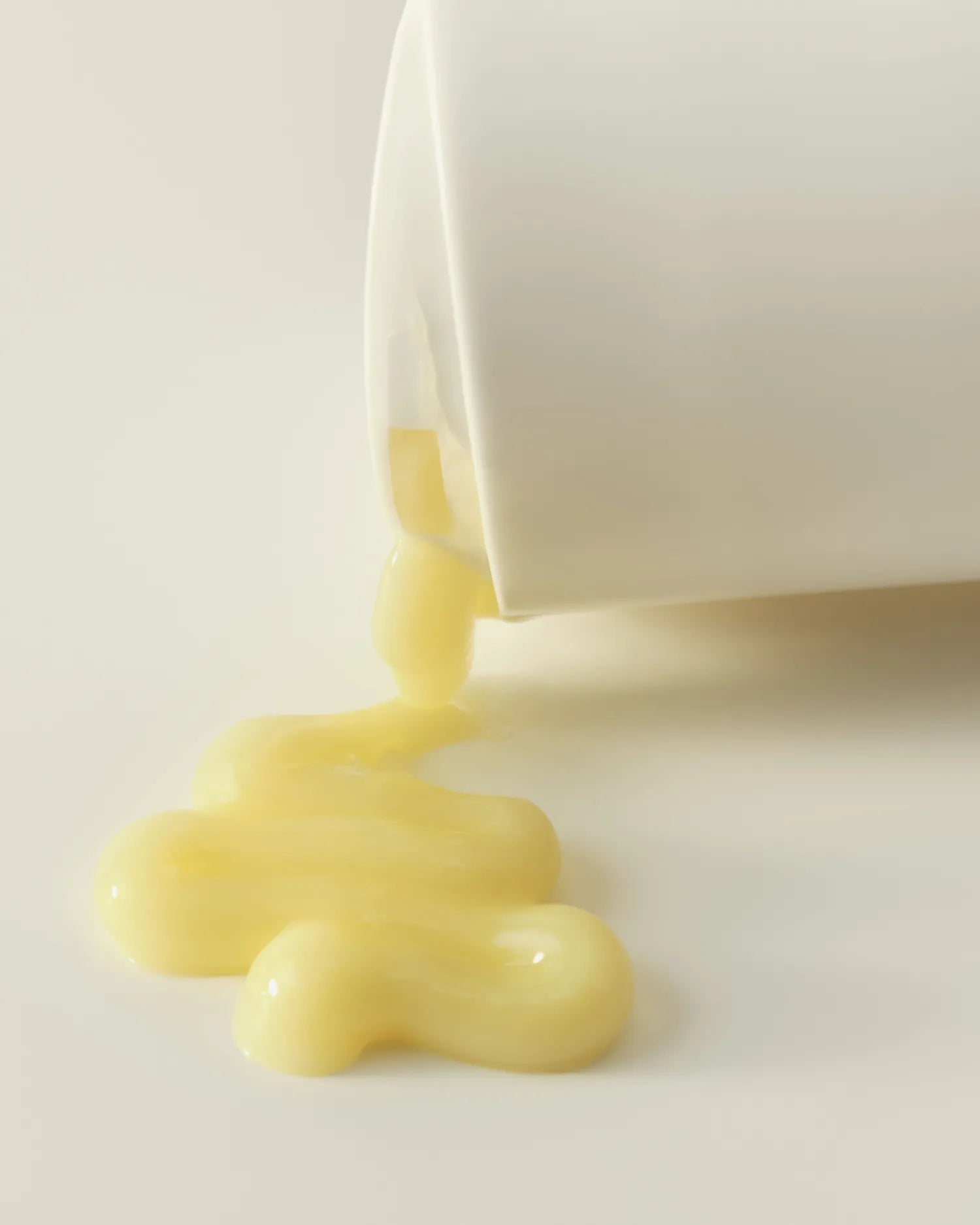 White tube dispenser pouring pale yellow liquid cleanser onto neutral background.