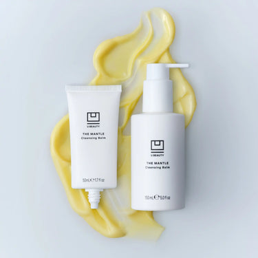 Two white bottles of The Mantle Cleansing Balm with yellow swirled texture behind them.