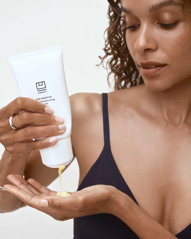 Person with curly hair dispensing white conditioning wash from tube into palm of hand.
