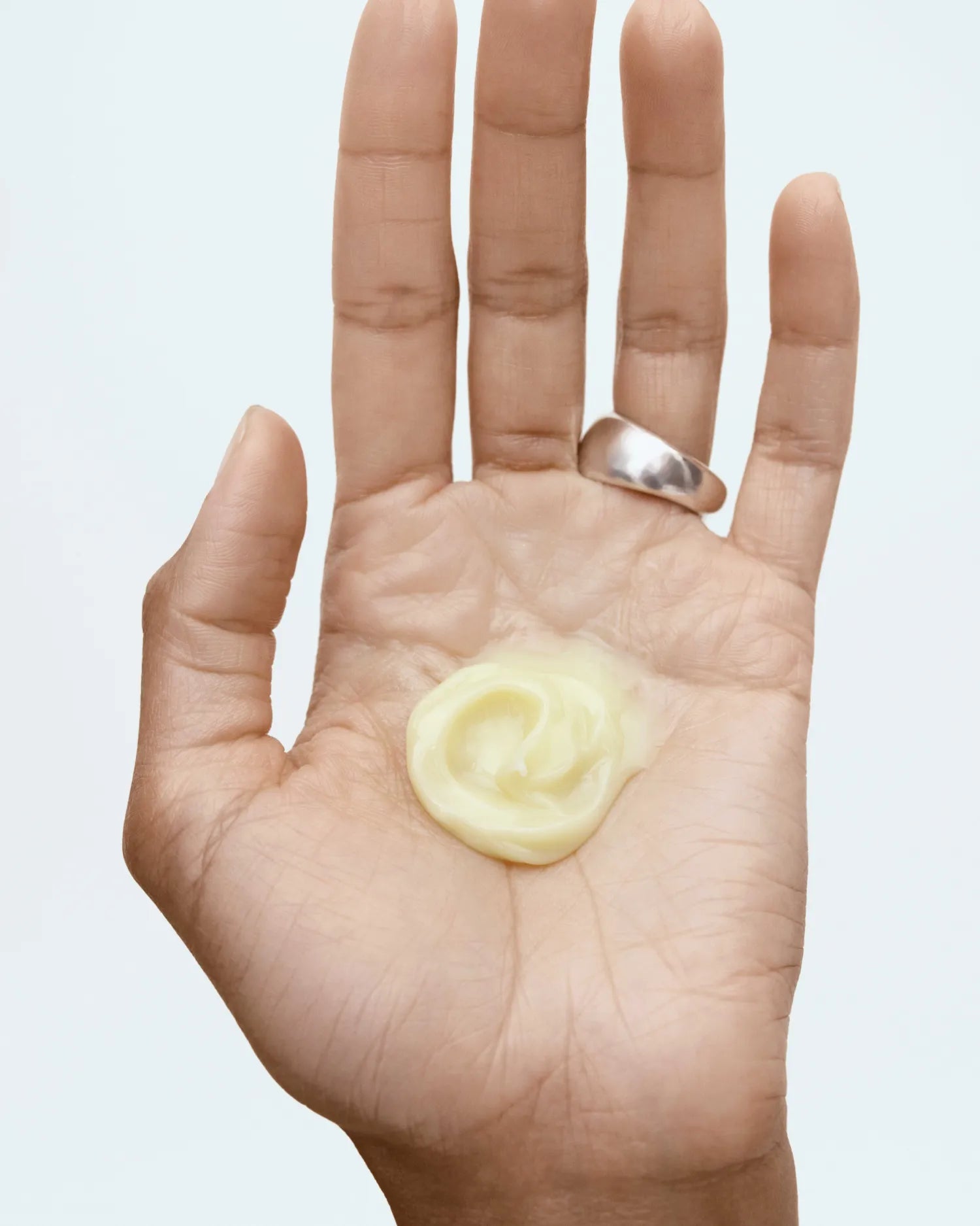 Open palm displaying a pale yellow cleansing product with a silver ring on the finger.