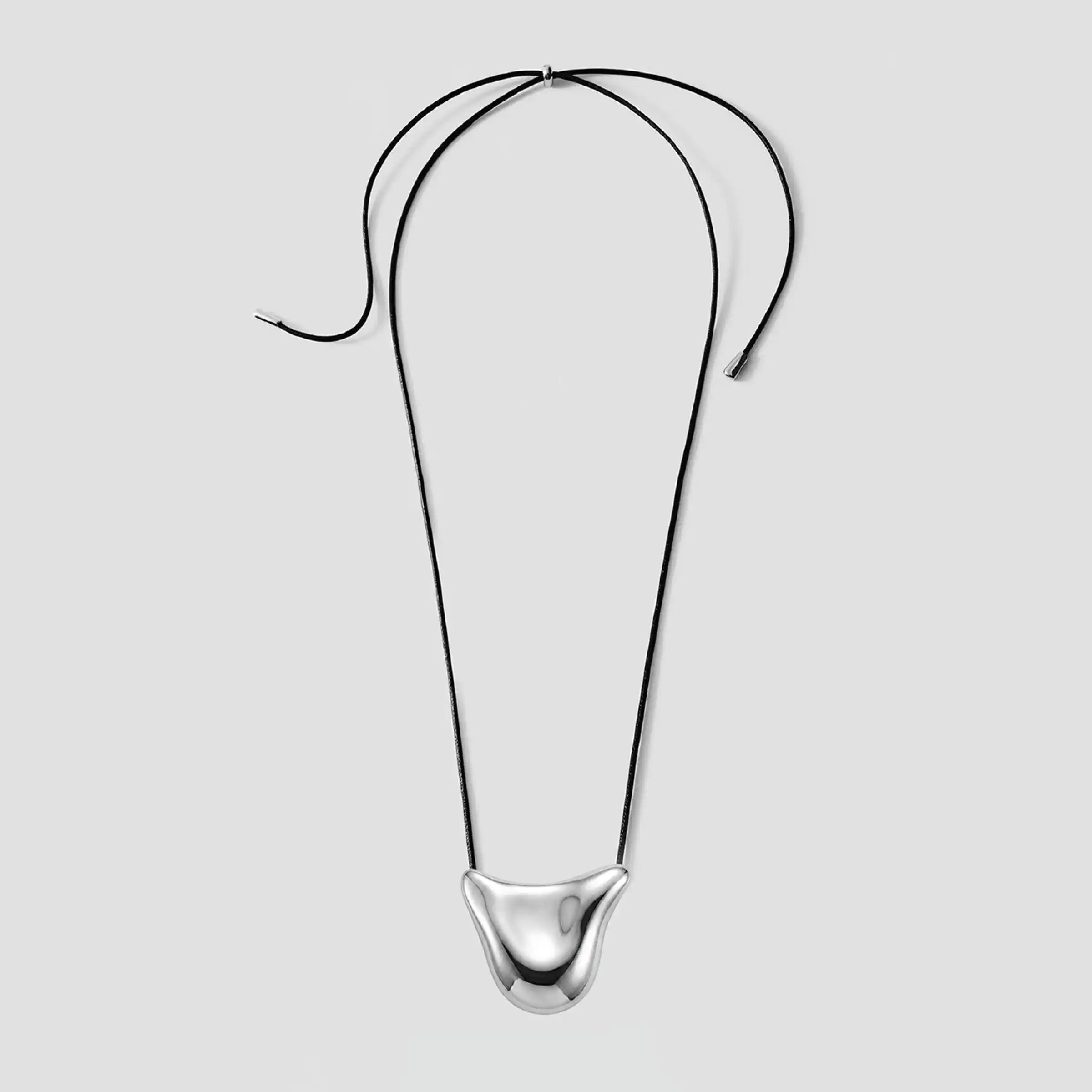 Collier en fil métallique noir courbé, orné d'un pendentif sculptural en argent poli au centre, dans la partie inférieure.