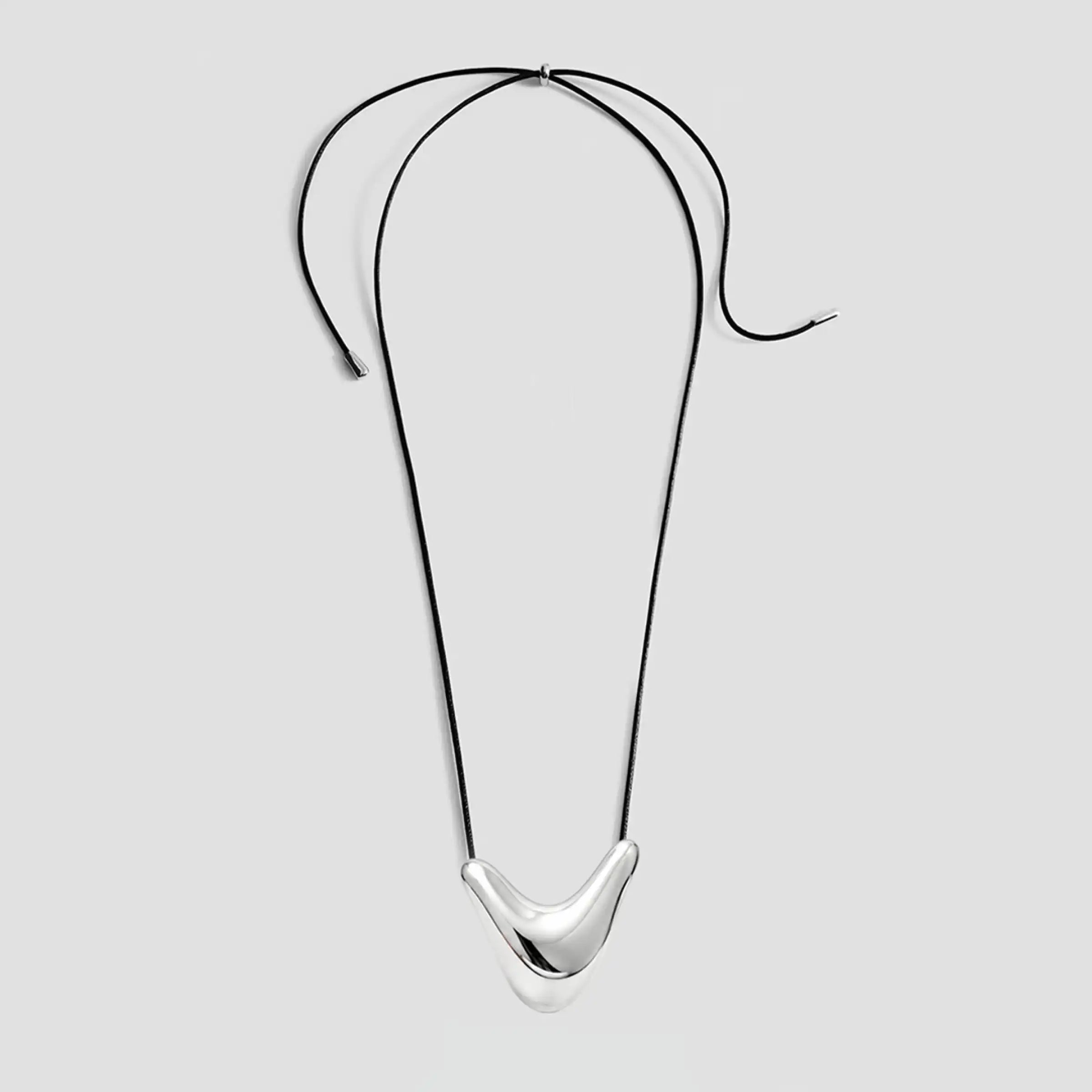 Collier en cordon noir orné d'un pendentif incurvé en argent poli au centre, présenté à plat sur un fond blanc.