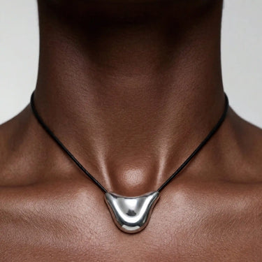 Collier composé d'un pendentif incurvé en argent monté sur un fin cordon noir, porté près du cou.