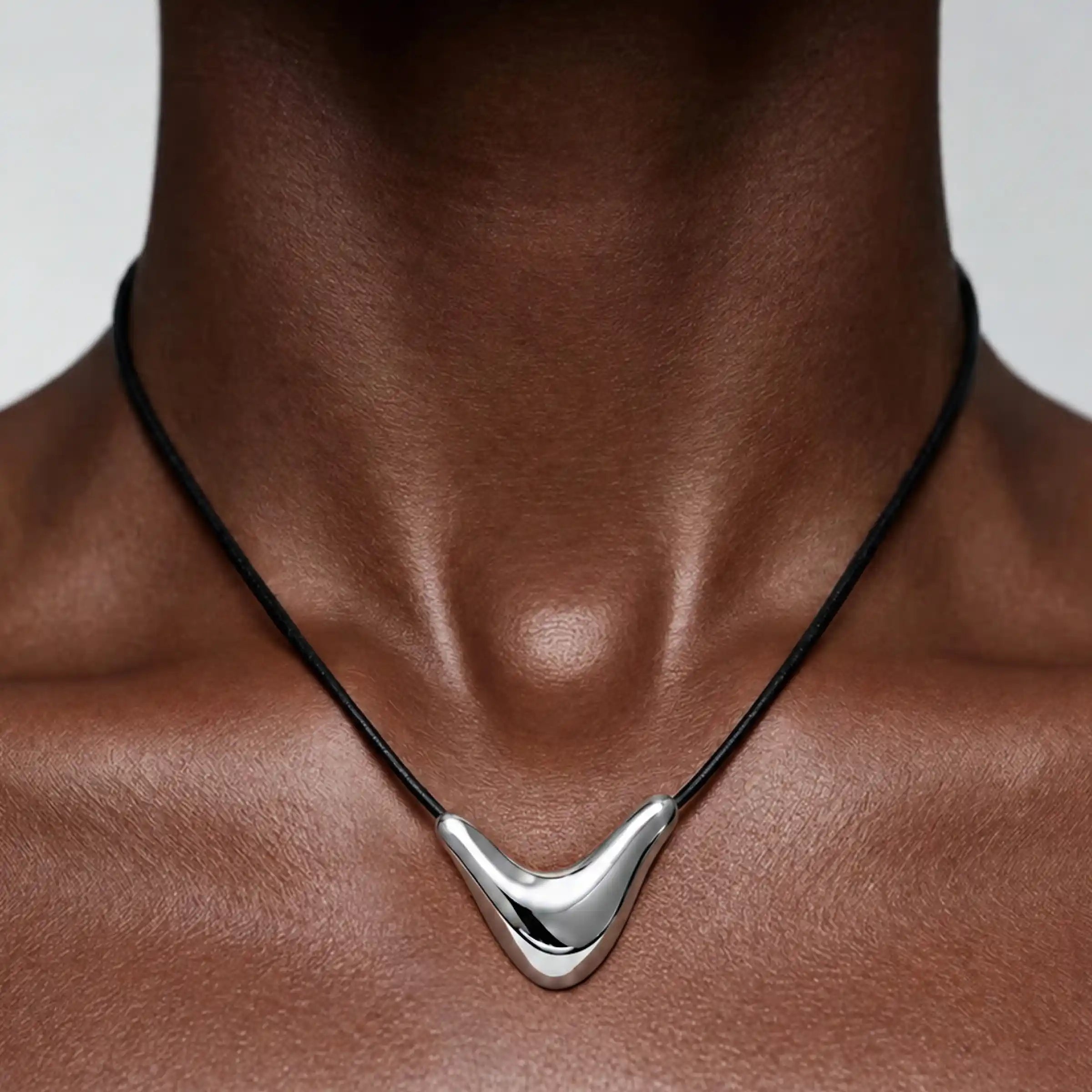 Collier composé d'un pendentif argenté incurvé monté sur un cordon noir, porté au niveau de la clavicule.