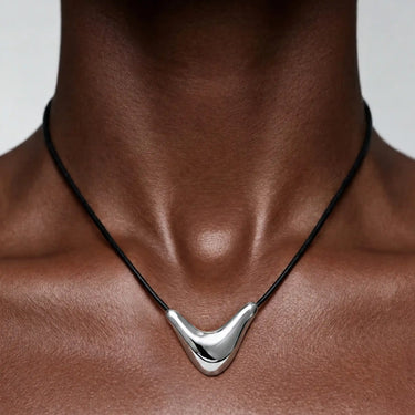 Collier composé d'un pendentif argenté incurvé monté sur un cordon noir, porté au niveau de la clavicule.