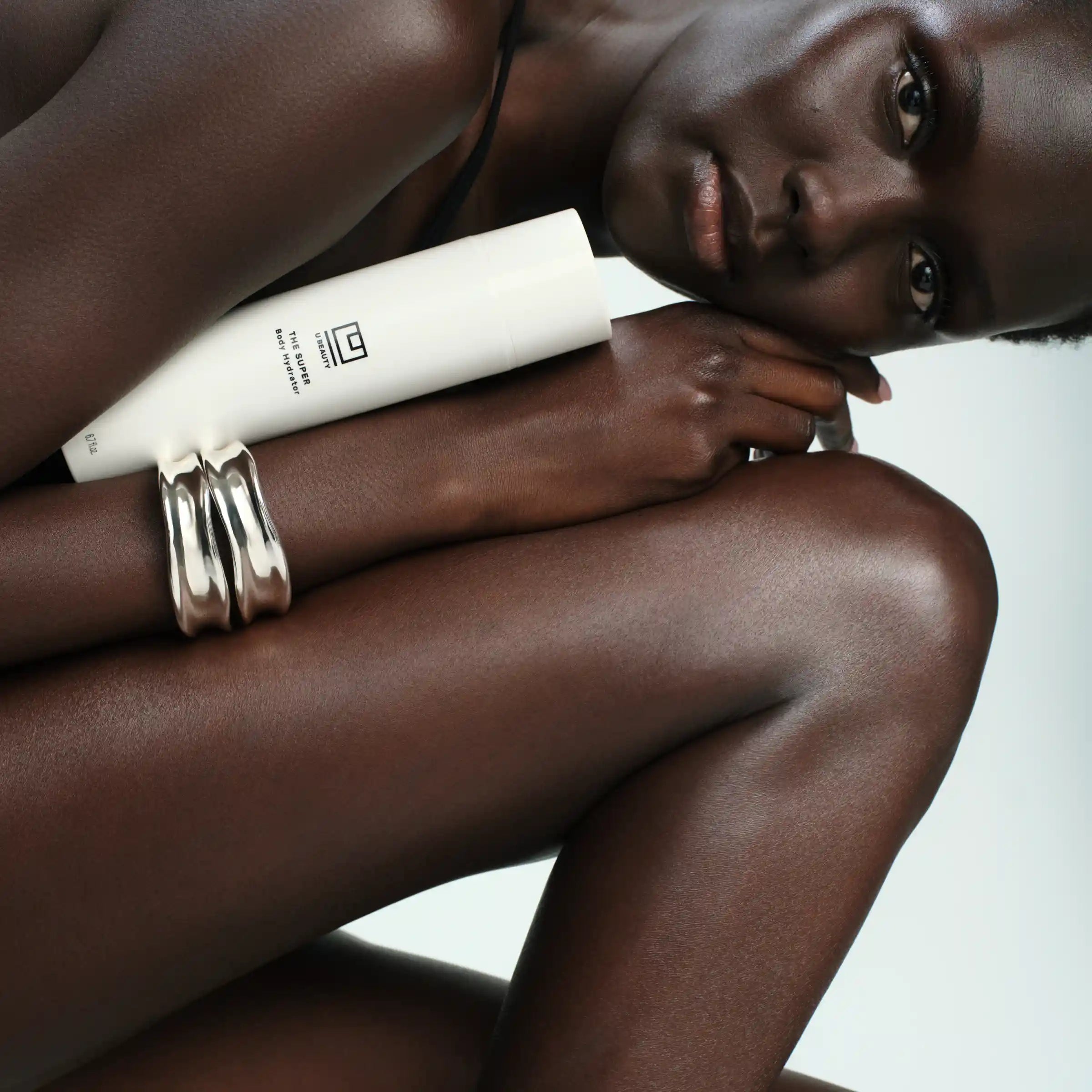 White moisturizer tube held against person's arm with silver bangles visible.