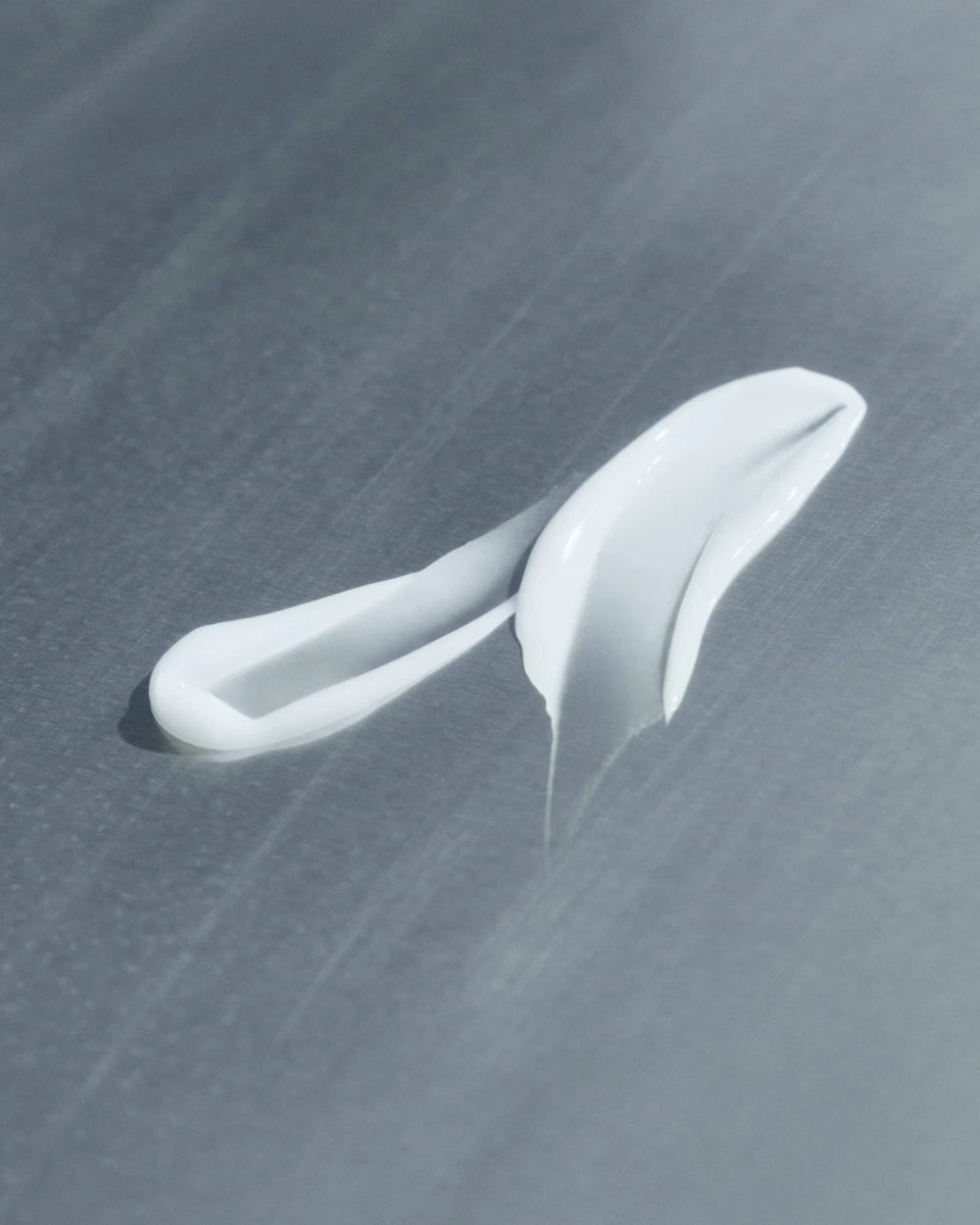 White facial serum with curved applicator on gray textured background.