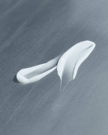 White facial serum with curved applicator on gray textured background.